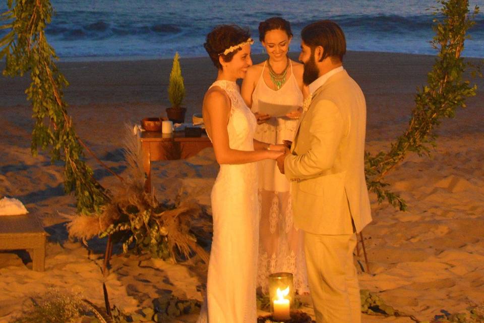 Novios frente a un círculo de follaje verde en la playa
