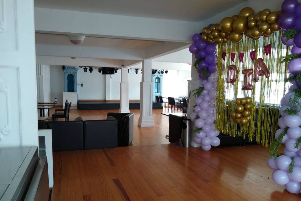 Salón decorado con globos morados, lilas y dorados