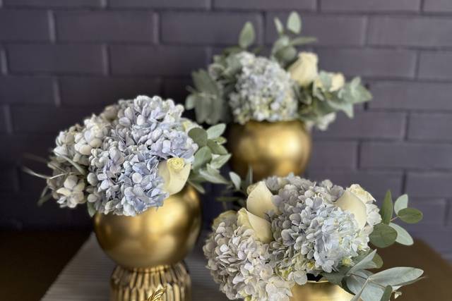 Arreglo de mesa con recipientes dorados y flores azules